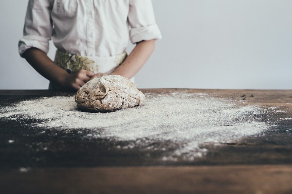 Iemand kneedt brooddeeg op een bebloemde houten tafel