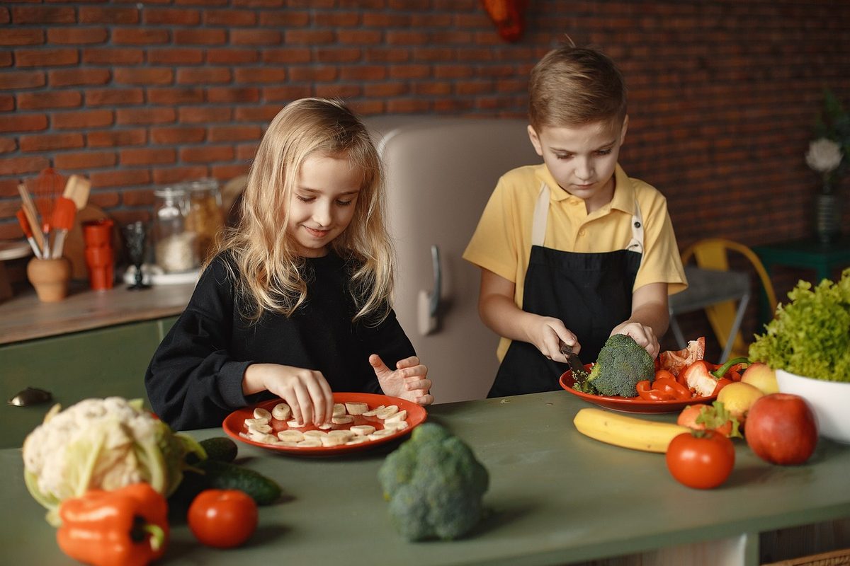 Twee kinderen snijden groente in de keuken