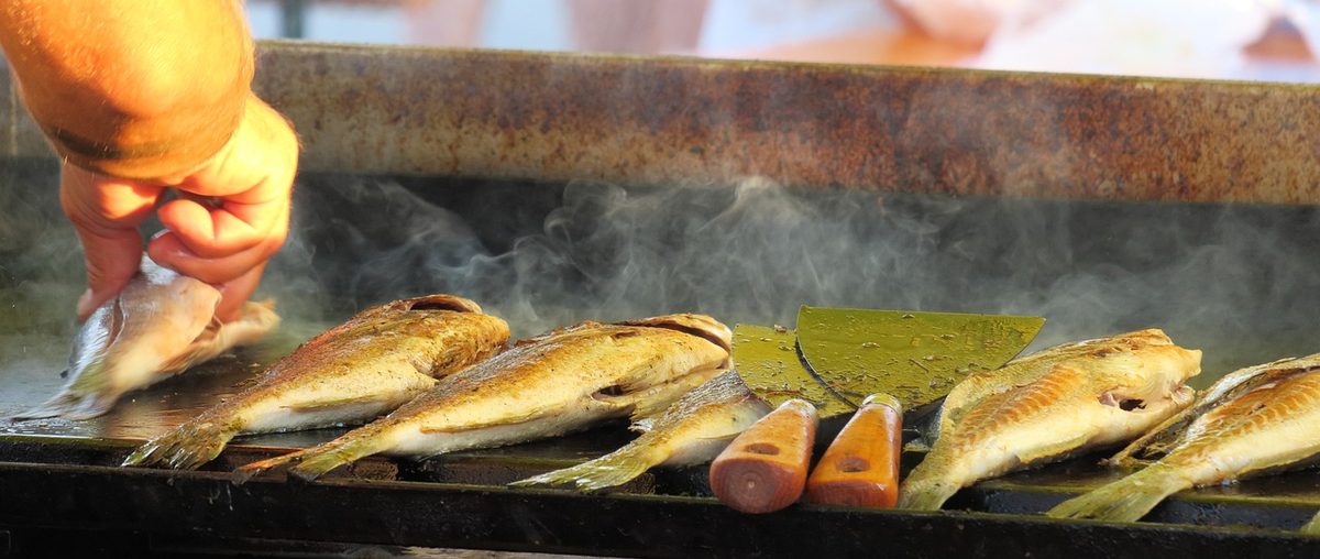 Hand keert grillende vis op een bakplaat