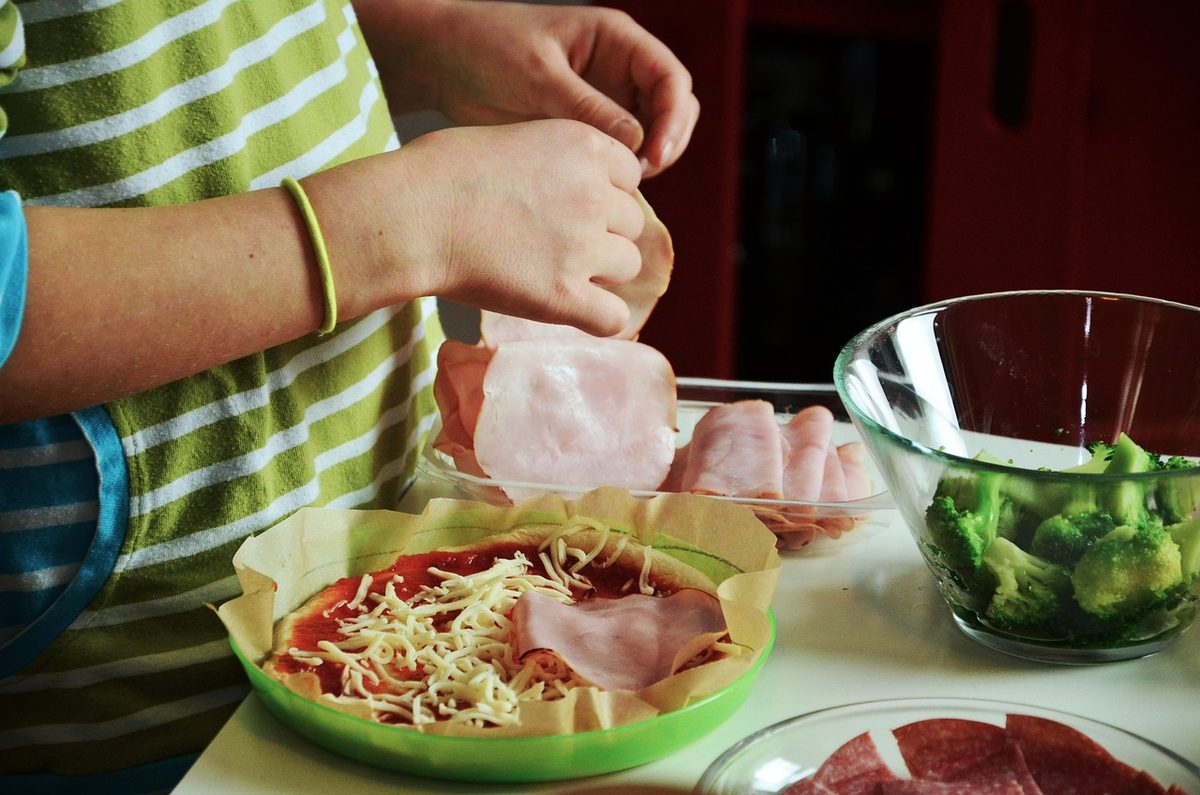 Iemand belegt een zelfgemaakte pizza met ham en kaas